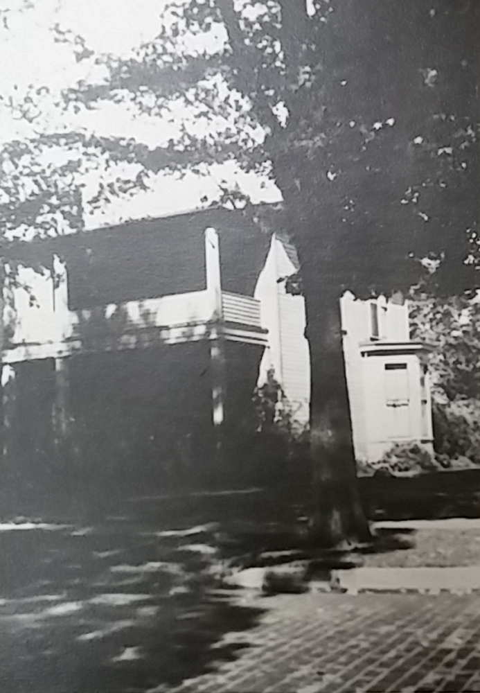 Black and white photograph of Zane Grey's childhood home in Zanesville, Ohio. Photo shows a partial view of a two-story white house with a large tree in front.