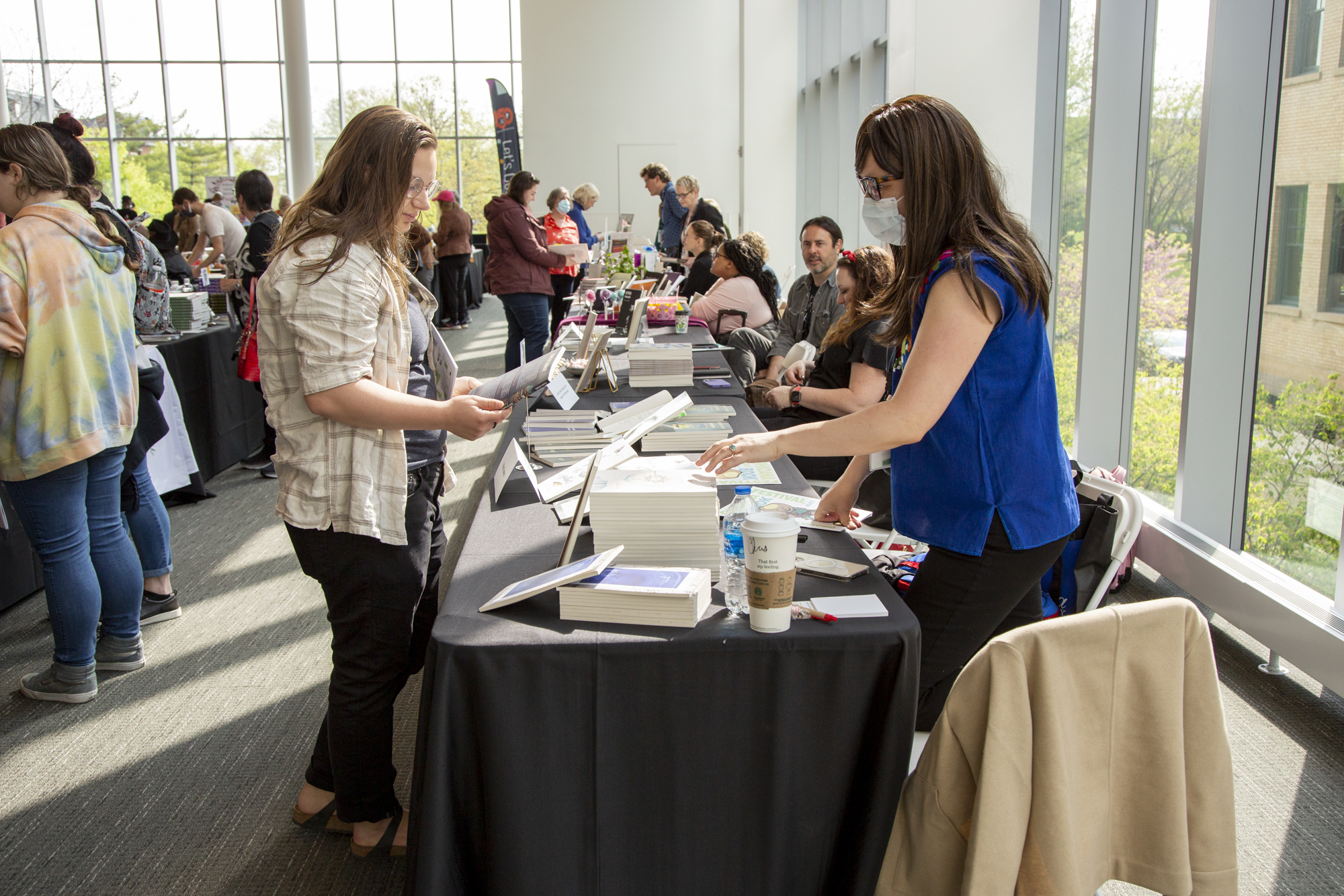 This image is from the 2023 Ohioana Book Festival. It shows Ohio Author Felicia Zamora connecting with a reader, who is looking at Zamora's various poetry books. The background includes other festival attendees.